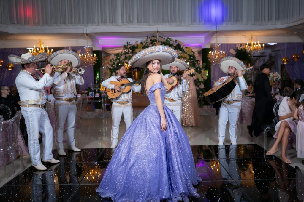 Woman in purple dress dances with mariachi band at festive indoor Mexican celebration.
