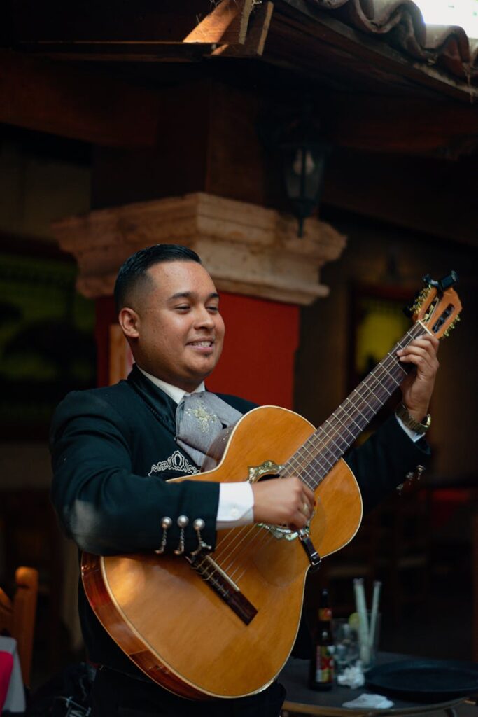 A smiling mariachi musician plays an acoustic guitar outdoors, capturing the essence of Mexican culture.